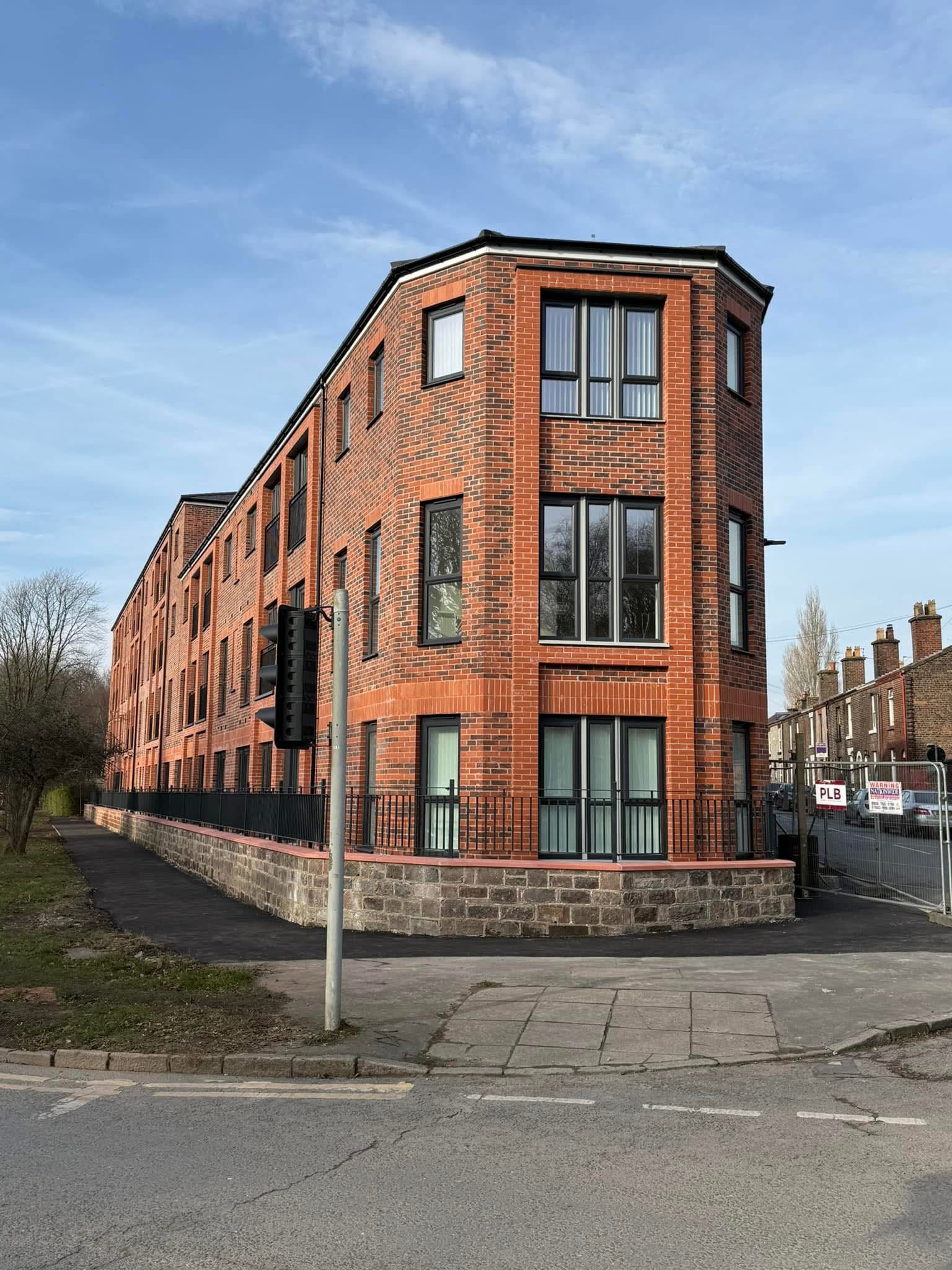 Completed brick apartment building with perimeter railings and paved frontage.