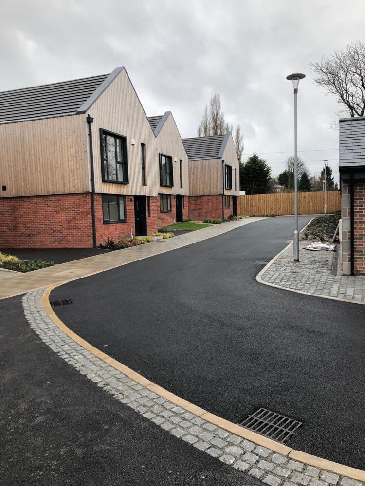 A newly surfaced estate road with granite sett channels and block-paved footways serving new houses.