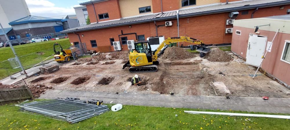 A P3 Plant excavator digging foundation pads alongside a healthcare building, with a dumper and a groundworker on site.