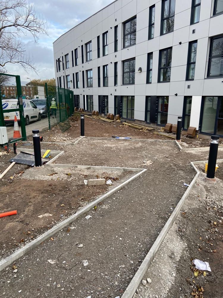 New kerbed footpaths and bollard lighting being laid outside a completed three-storey office building.